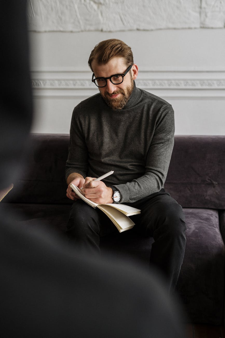 man in gray sweater and black pants sitting on purple couch